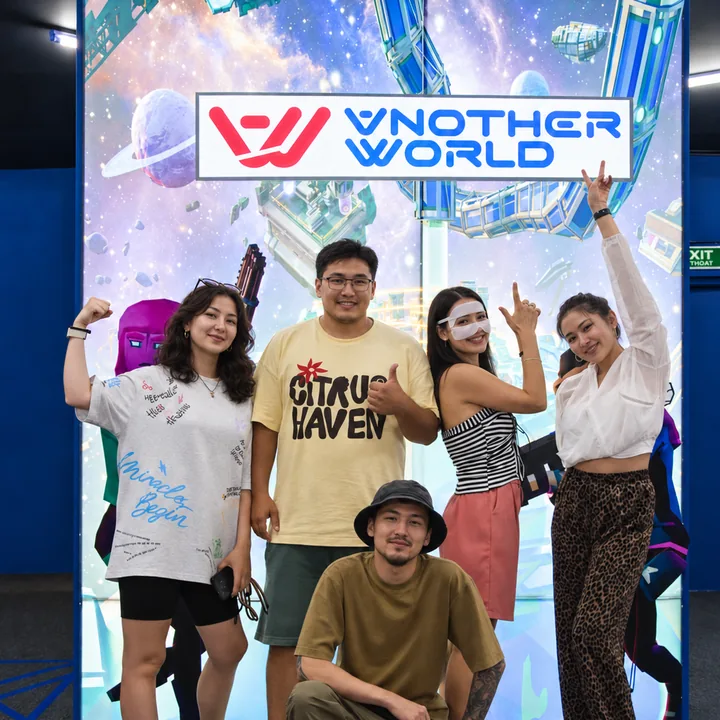 Five guests pose for a group photo beneath the illuminated logo at Another World Da Nang.
